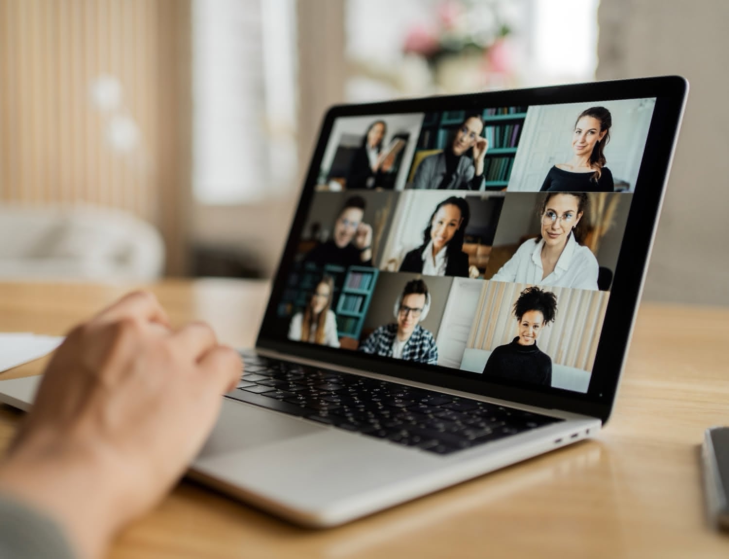 Laptop z widokiem galerii uczestników spotkania online, dłoń na klawiaturze